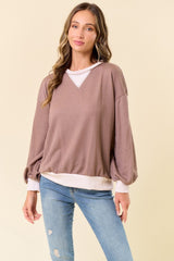 woman wearing a taupe oversized sweatshirt with balloon sleeves and a white trim, paired with light blue jeans