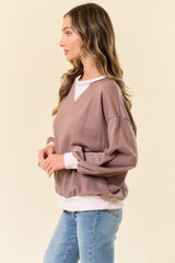 woman wearing a taupe oversized sweatshirt with a white neckline and cuffs, paired with light blue jeans