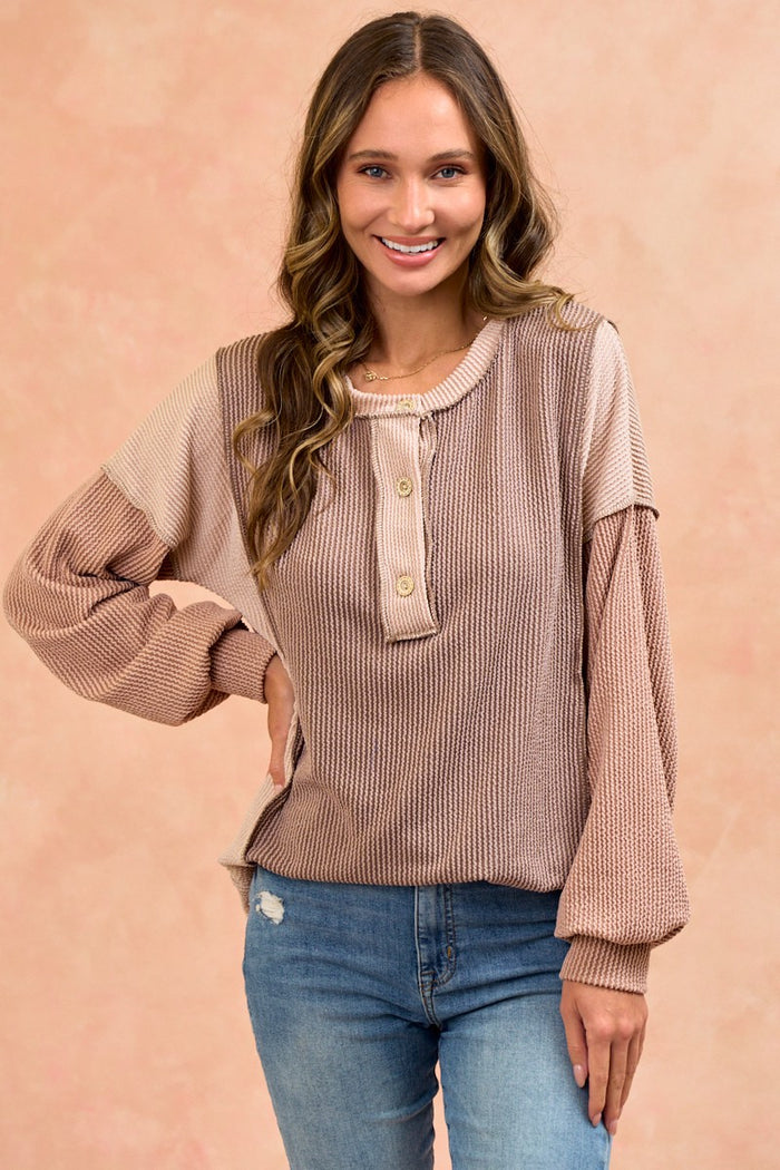 woman wearing a color-blocked ribbed knit long sleeve top with button details and a relaxed fit, paired with denim jeans