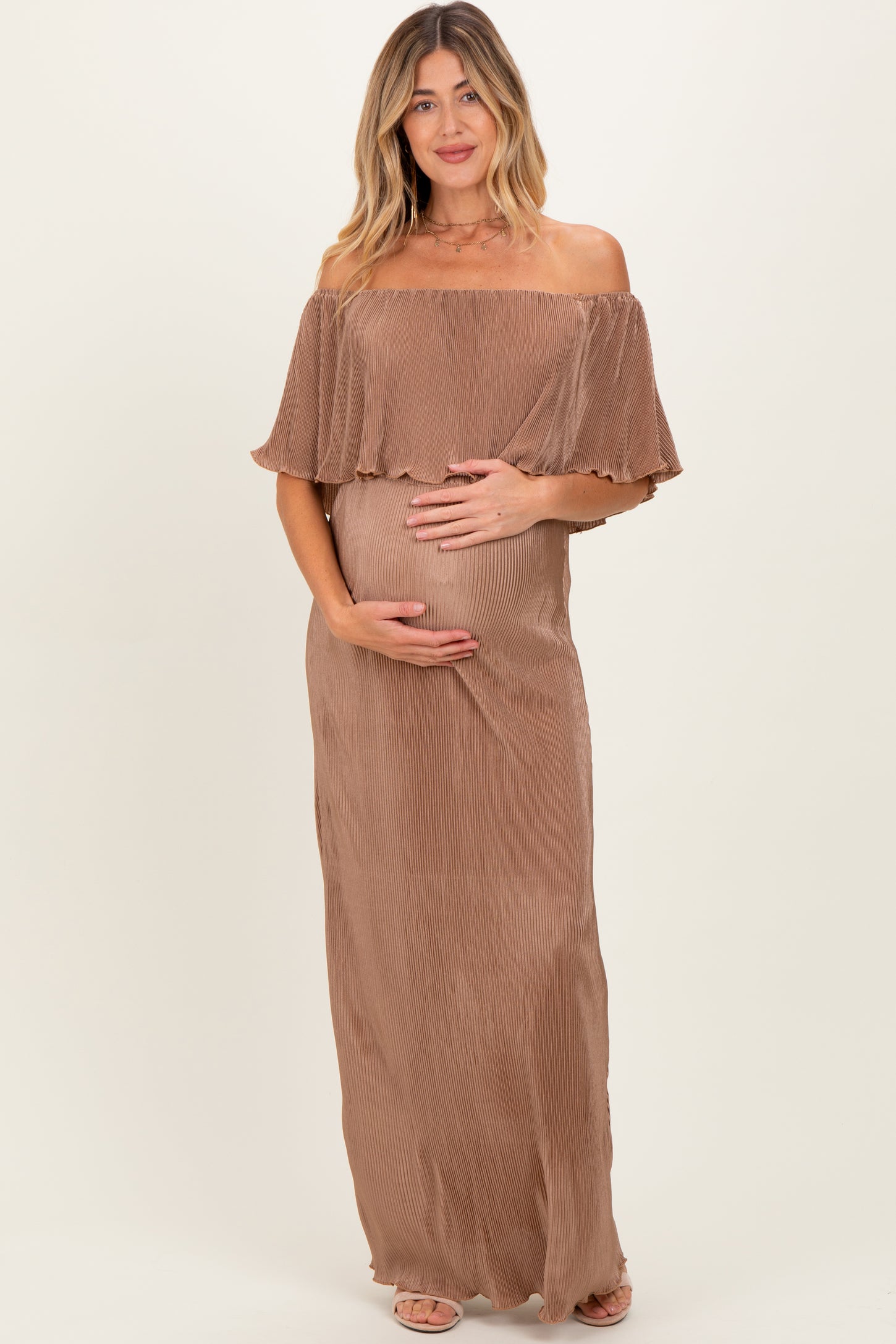 woman wearing a brown off-shoulder maternity dress with ruffle detailing and holding her baby bump