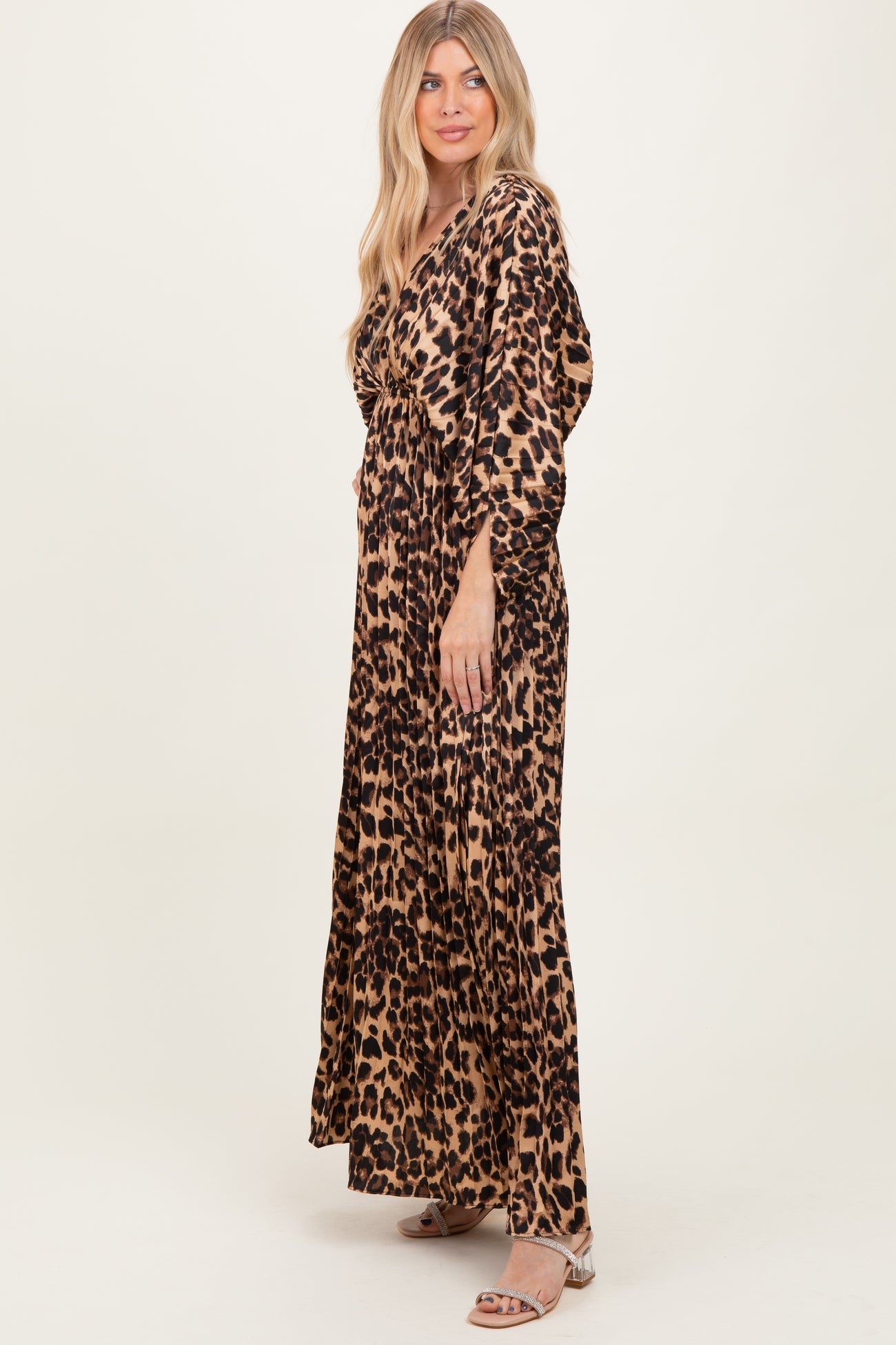 woman wearing a leopard print maxi dress with a wrap style and long sleeves, standing sideways against a neutral background
