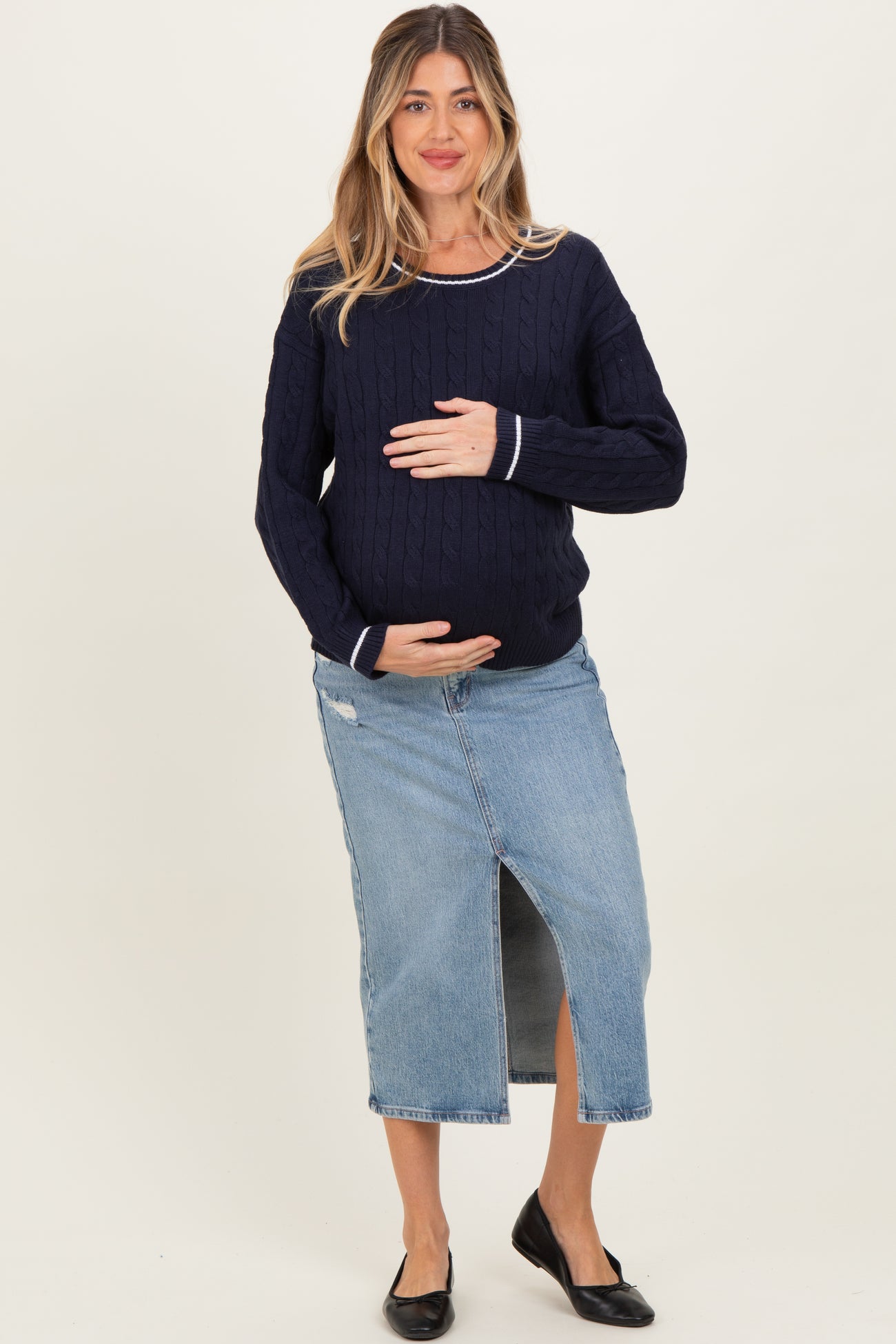 woman wearing a navy maternity sweater and a denim midi skirt, holding her baby bump