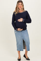 woman wearing a navy maternity sweater and a denim midi skirt, holding her baby bump