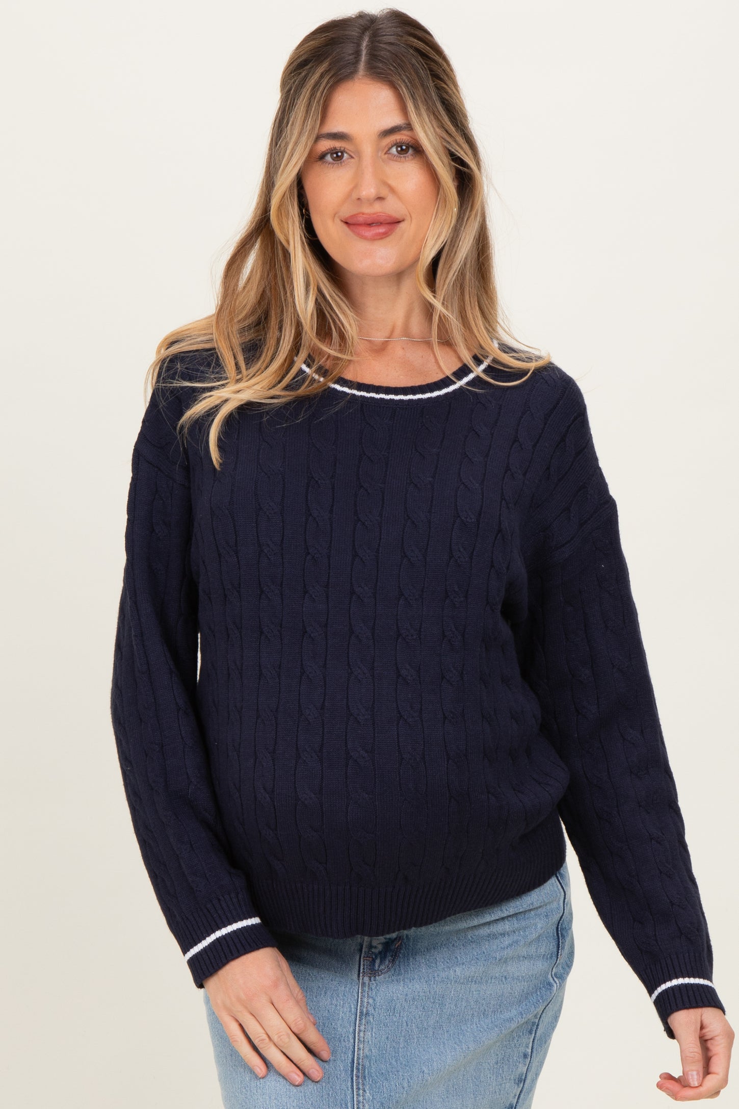 woman wearing a navy blue cable knit maternity sweater with white trim and a visible baby bump
