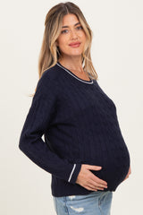 woman wearing a navy blue cable knit maternity sweater with white trim and holding her baby bump