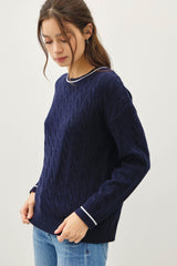 woman wearing a navy blue cable knit sweater with white trim and light blue jeans
