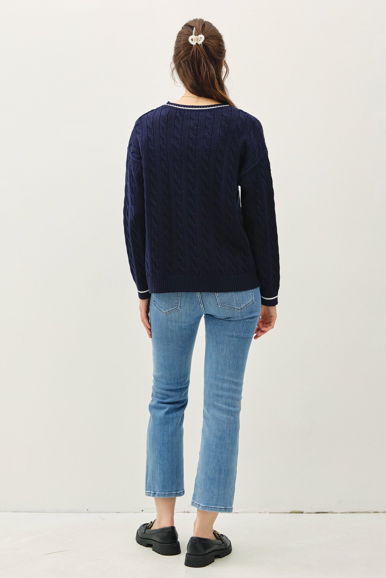 woman wearing a navy blue cable knit sweater and light blue cropped jeans, view from the back