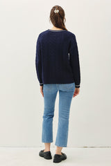 woman wearing a navy blue cable knit sweater and light blue cropped jeans, view from the back