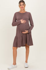 woman wearing a mauve ribbed long sleeve maternity dress with a tiered skirt and holding her baby bump