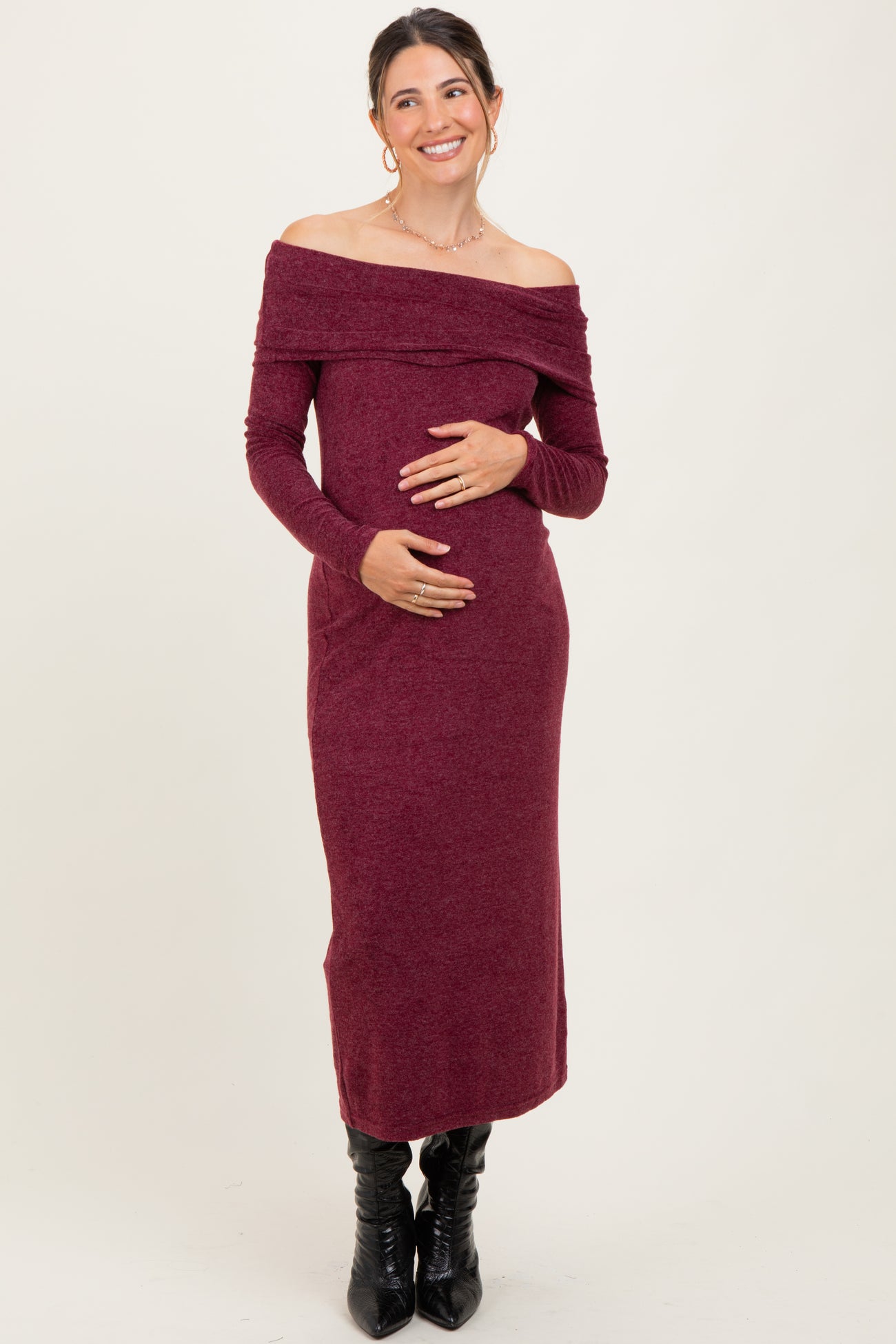 woman wearing a burgundy off-shoulder maternity dress and holding her baby bump