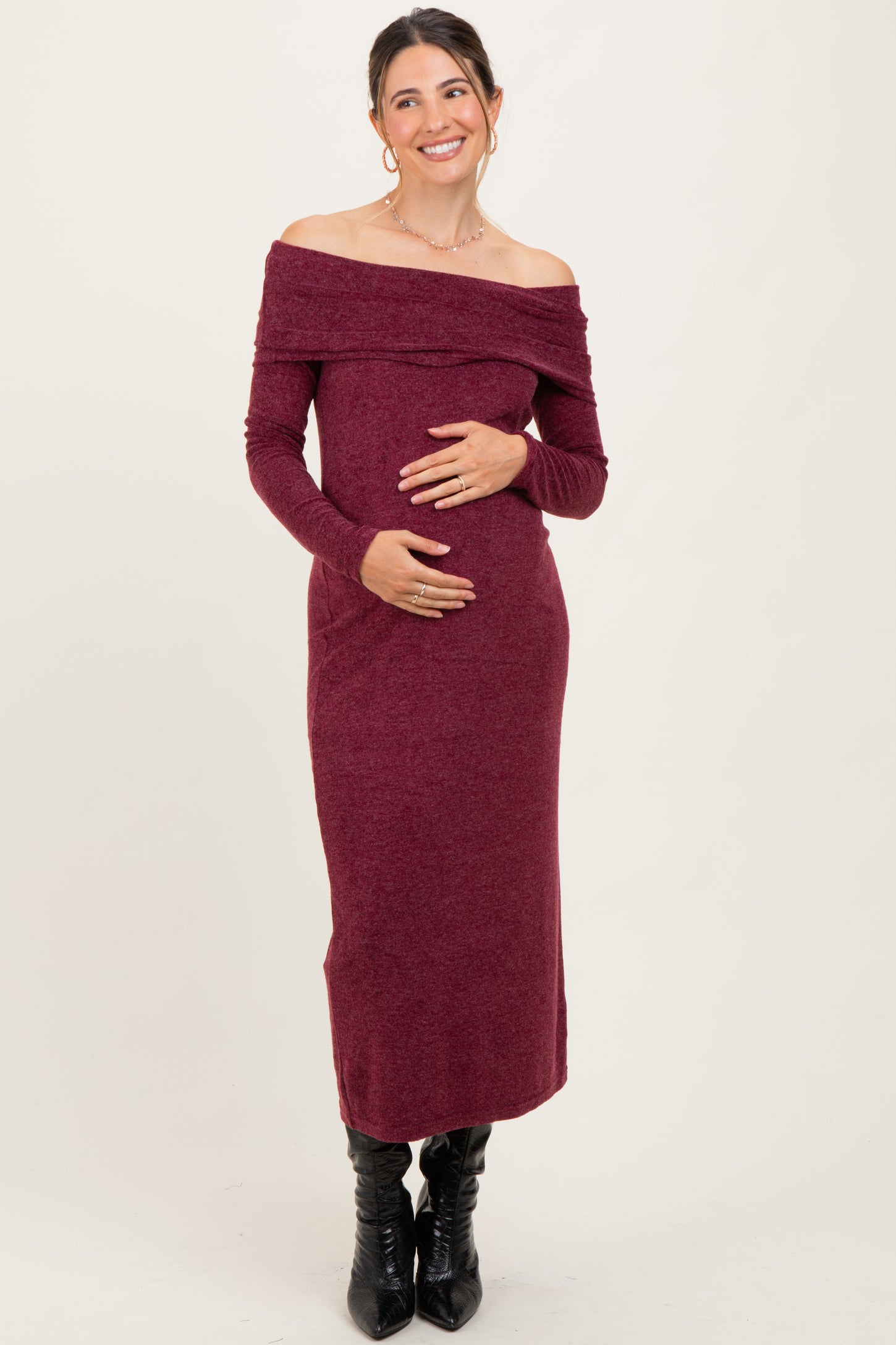 woman wearing a burgundy off-shoulder maternity dress and holding her baby bump