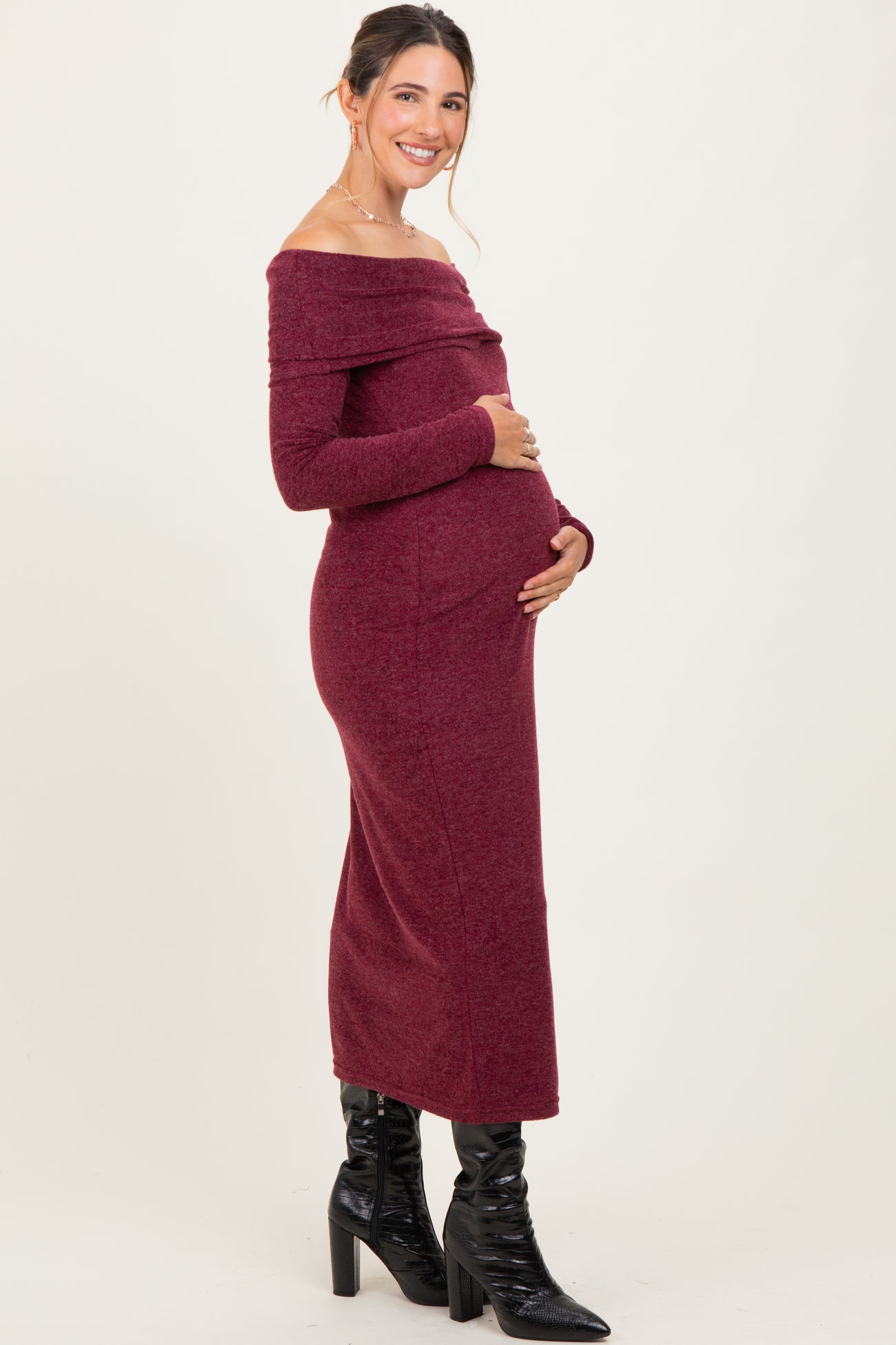 woman wearing a burgundy off-the-shoulder maternity dress and cradling her baby bump