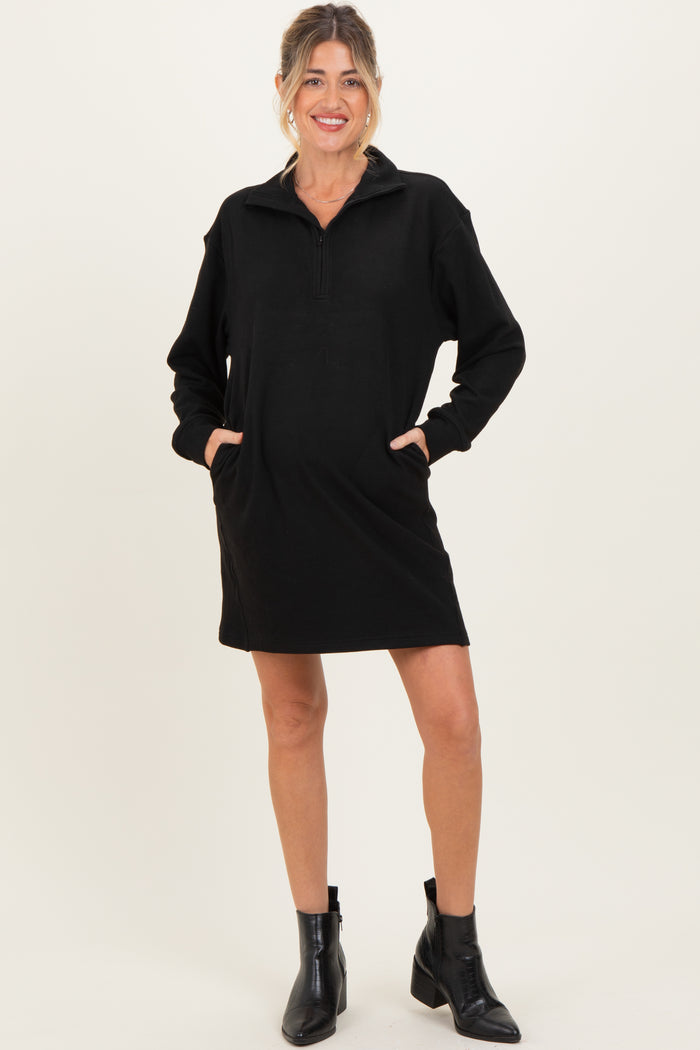 woman wearing a black maternity pullover dress with a quarter zip and two front pockets