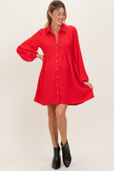 woman wearing a red maternity dress with a button-down front and bell sleeves, holding a baby bump