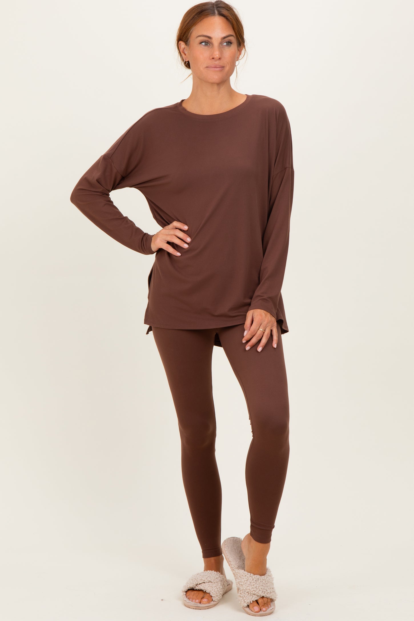 woman wearing a brown long sleeve lounge top with side slits and matching leggings, styled with fuzzy slippers