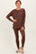 woman wearing a brown long sleeve lounge top with side slits and matching leggings, styled with fuzzy slippers