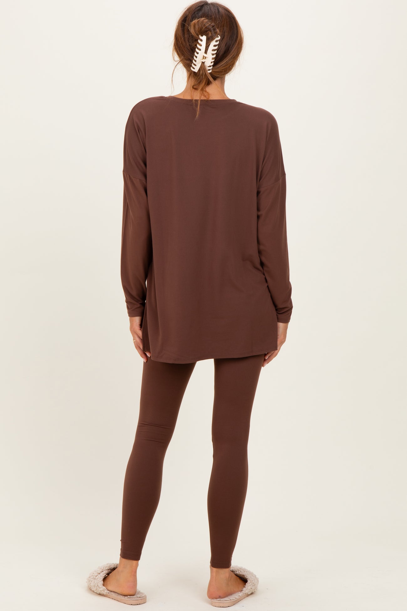 woman wearing a brown long sleeve top and matching leggings, seen from the back, with cozy slippers on