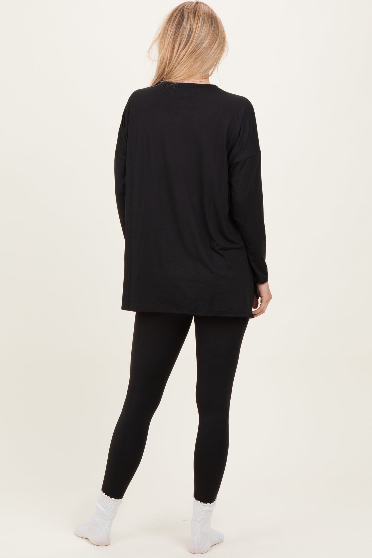 woman wearing a black oversized long sleeve top with black leggings and white socks, viewed from the back
