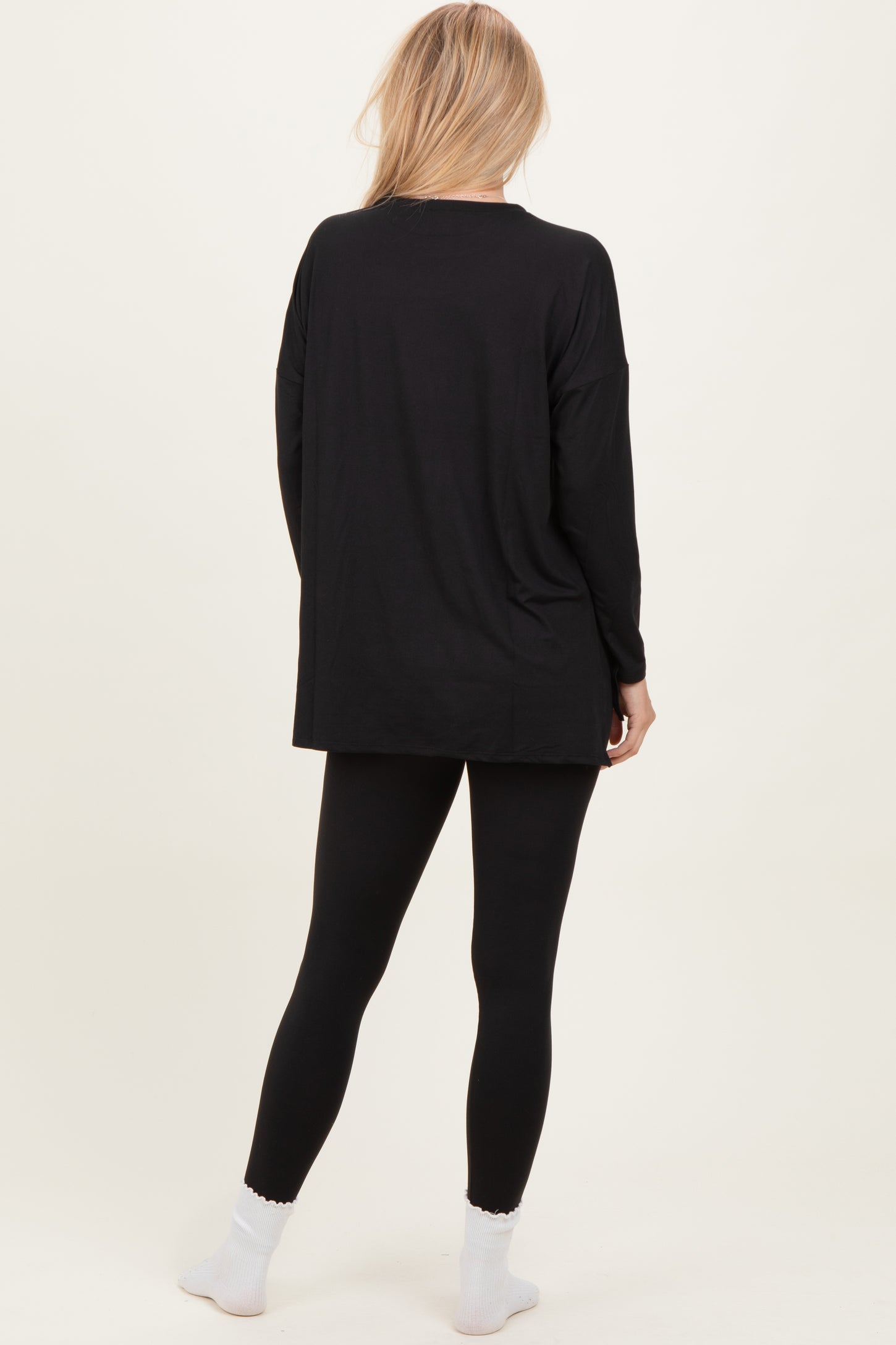 woman wearing a black oversized long sleeve top with black leggings and white socks, viewed from the back
