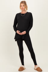woman wearing a black maternity long sleeve top and black leggings, showing her baby bump while standing