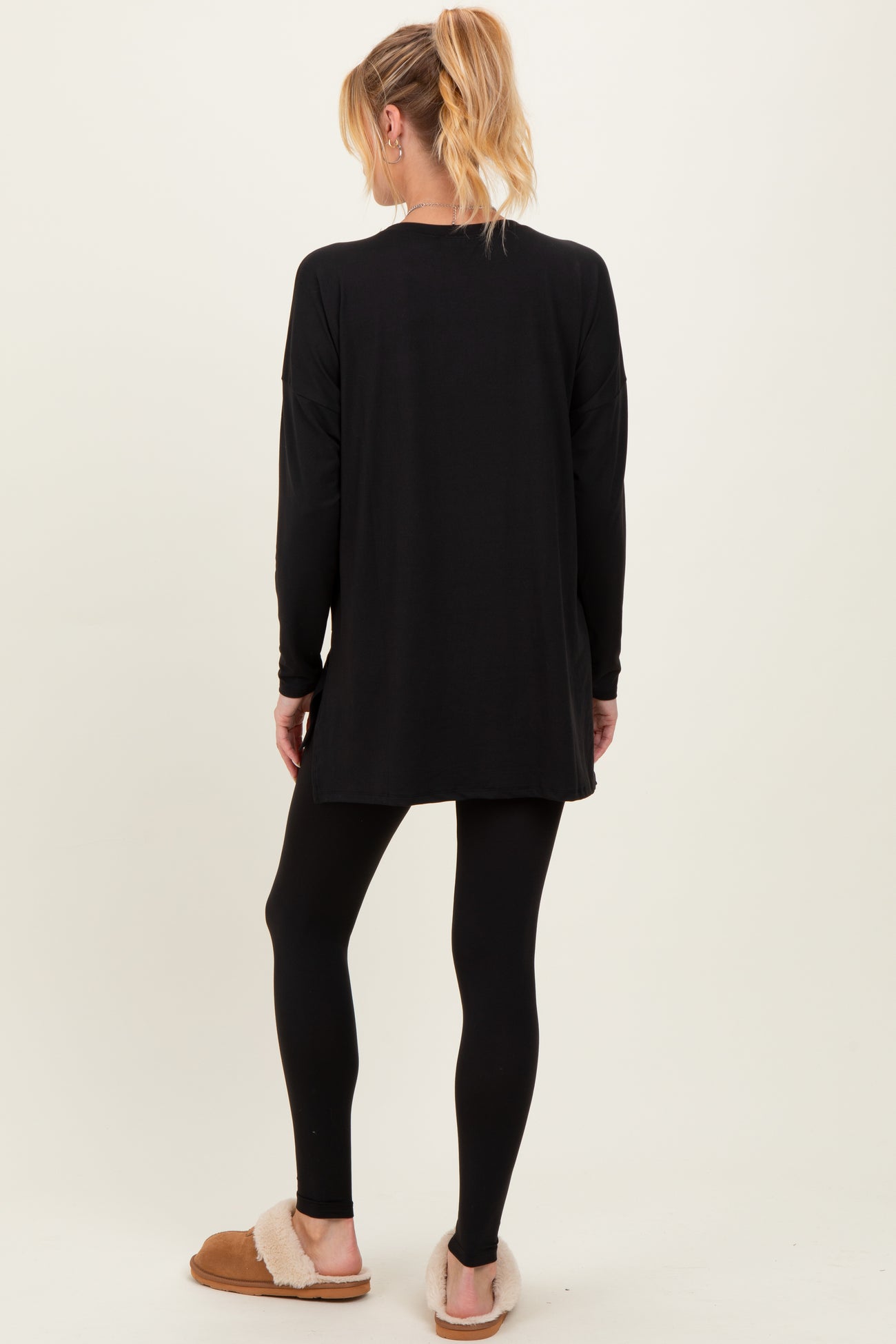 woman wearing a black long sleeve maternity top and black leggings, standing with her back to the camera