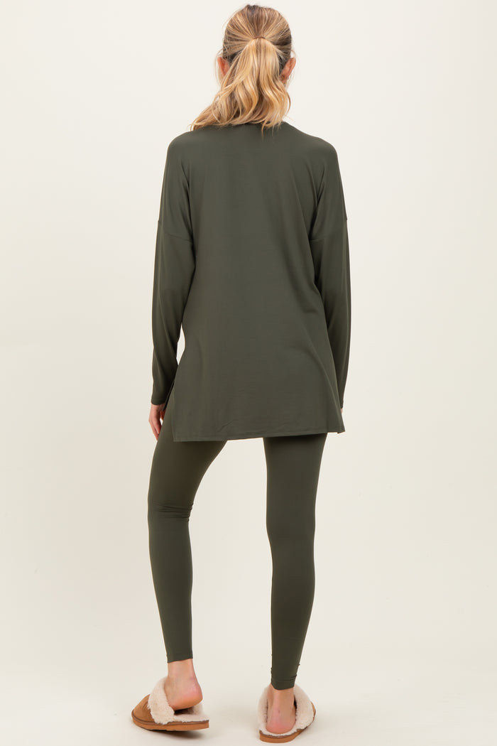woman wearing a dark green maternity top and matching leggings, facing away from the camera with long sleeves