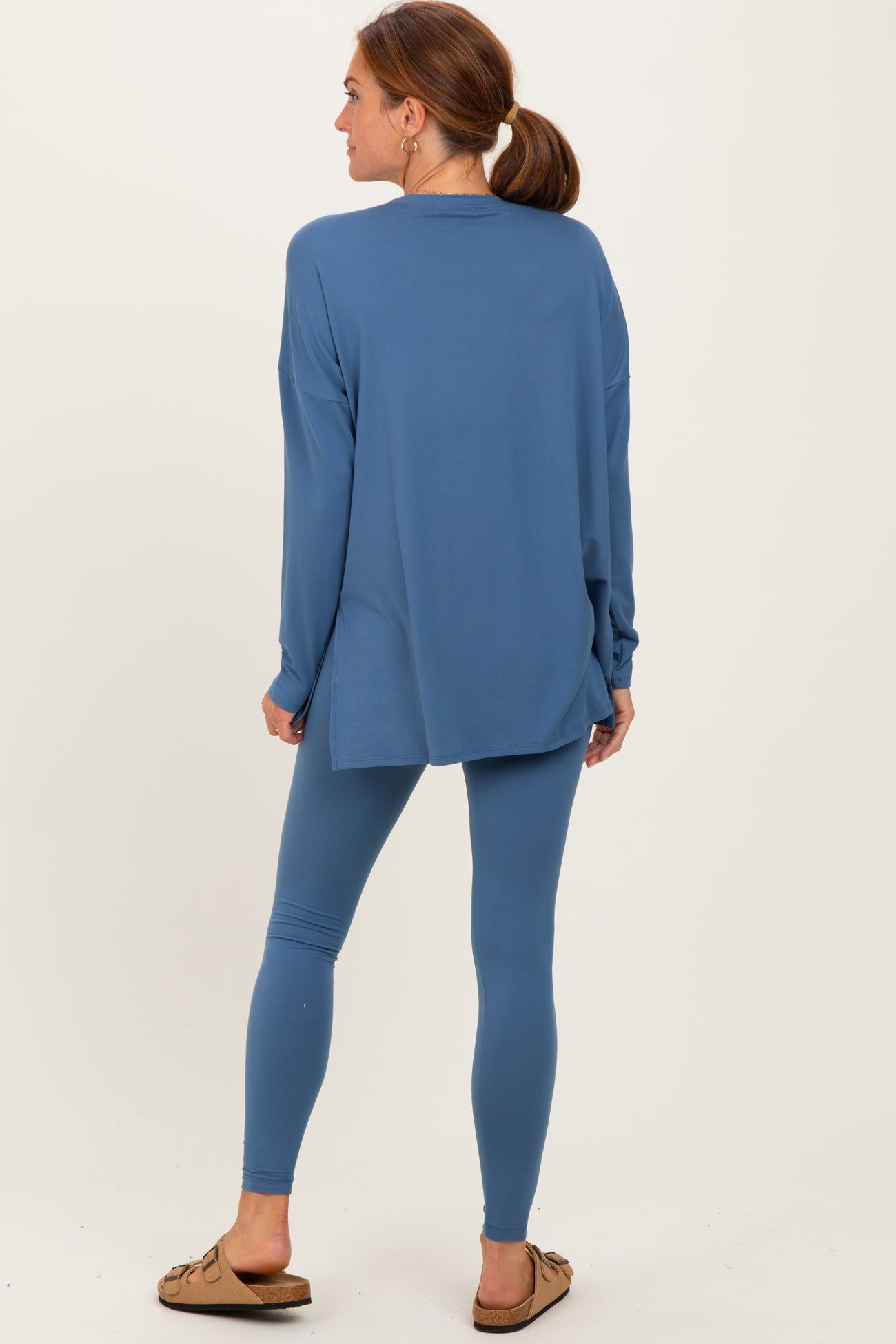 woman wearing a blue long sleeve top and matching leggings, standing with her back to the camera