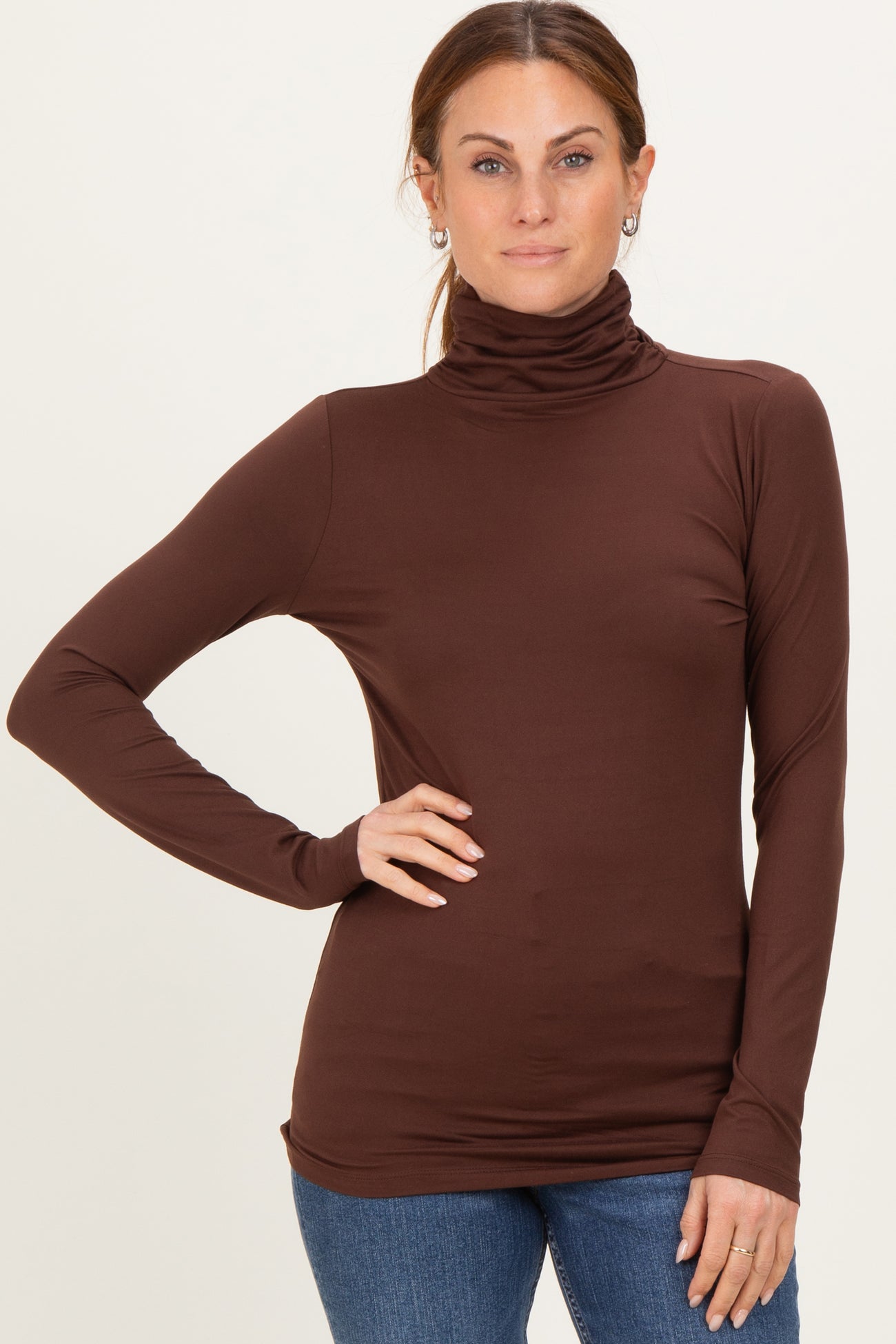 woman wearing a brown long sleeve turtleneck top with a fitted silhouette and subtle ruching details