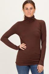 woman wearing a brown long sleeve turtleneck top with a fitted silhouette and subtle ruching details
