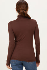 woman wearing a brown long sleeve turtleneck top, viewed from the back, paired with blue jeans