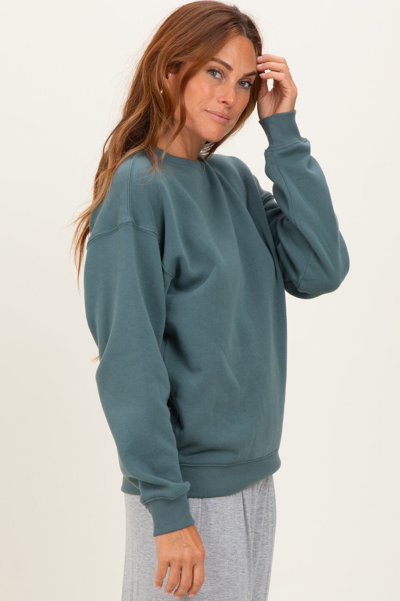 woman wearing a teal oversized sweatshirt with a crew neckline and relaxed fit, styled with gray bottoms