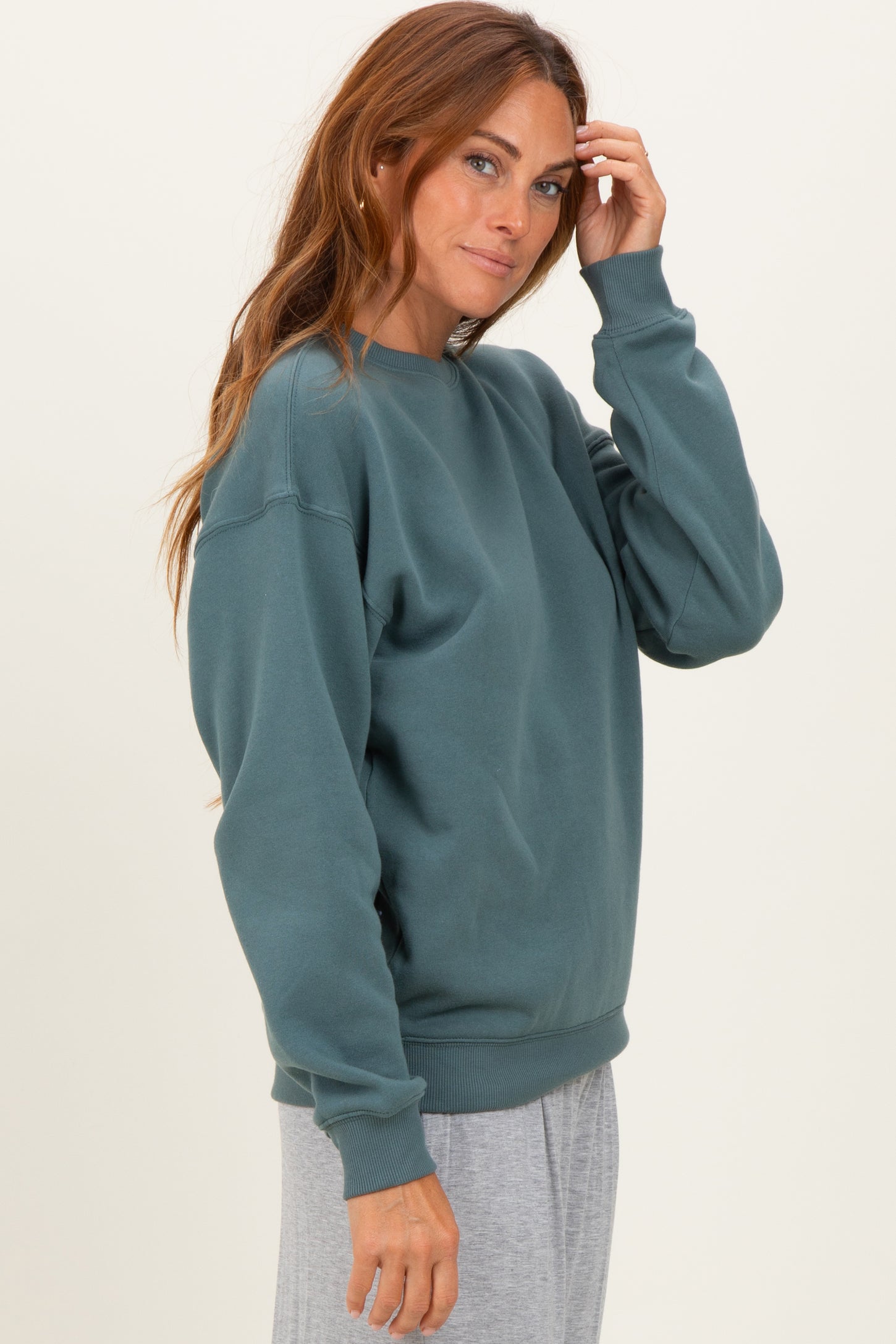woman wearing a teal oversized sweatshirt with a crew neckline and relaxed fit, styled with gray bottoms
