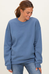woman wearing a relaxed fit blue sweatshirt with long sleeves and a round neckline, smiling and looking down