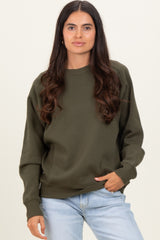 woman wearing an olive green oversized sweatshirt with a round neckline and relaxed fit, paired with light blue jeans