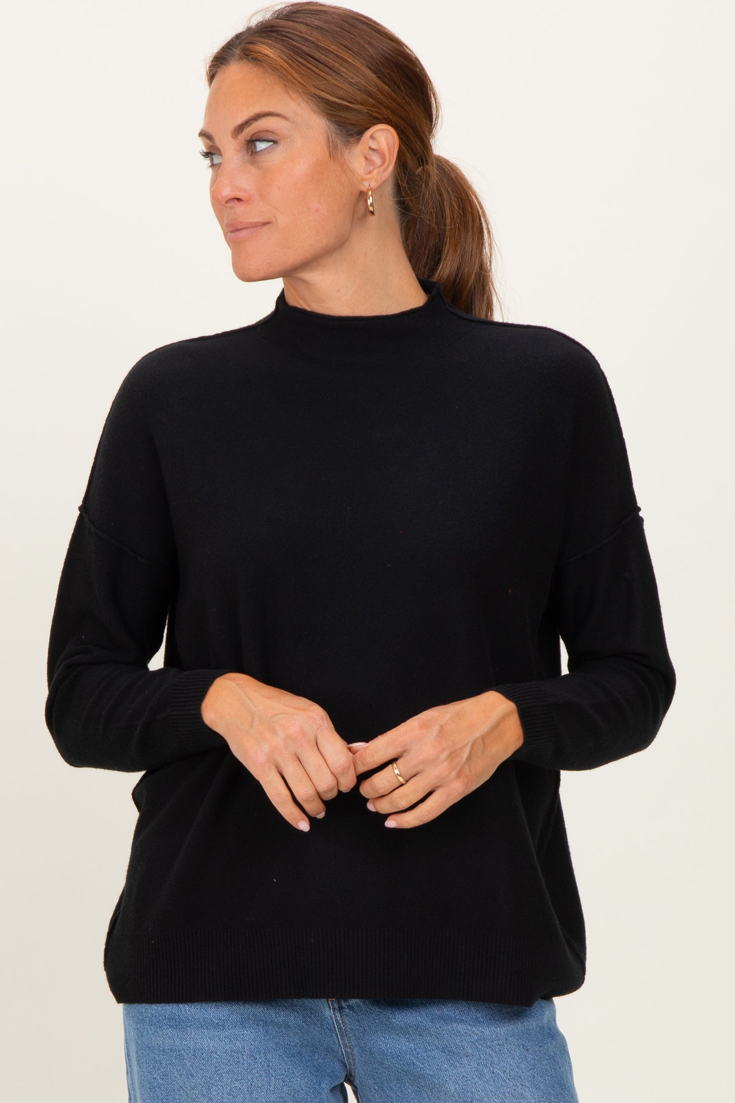 woman wearing a black long sleeve turtleneck sweater with a relaxed fit and side slits, styled with light blue jeans