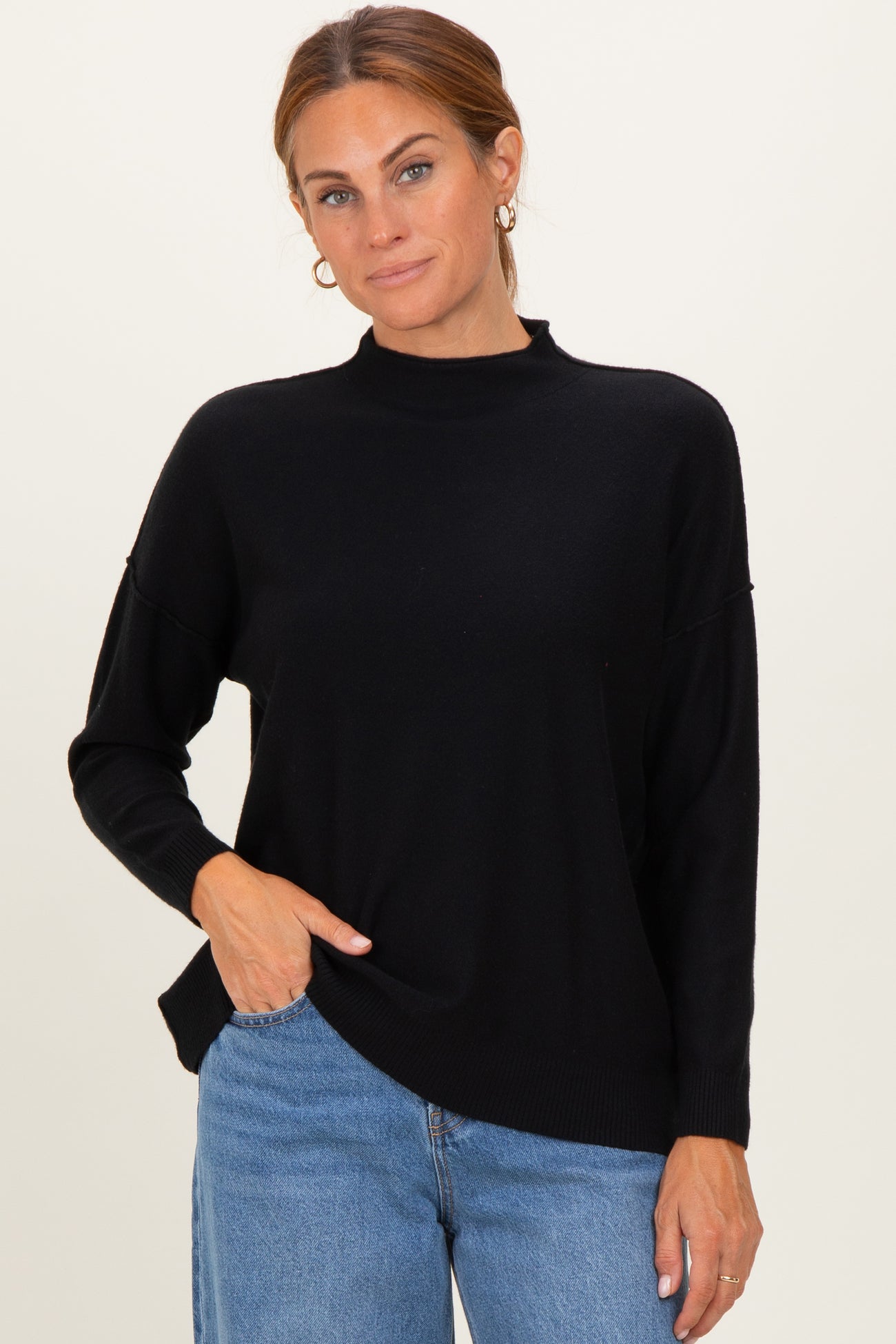 woman wearing a black mock neck sweater with dropped shoulders and side slits, paired with light blue jeans