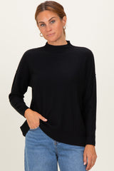 woman wearing a black mock neck sweater with dropped shoulders and side slits, paired with light blue jeans