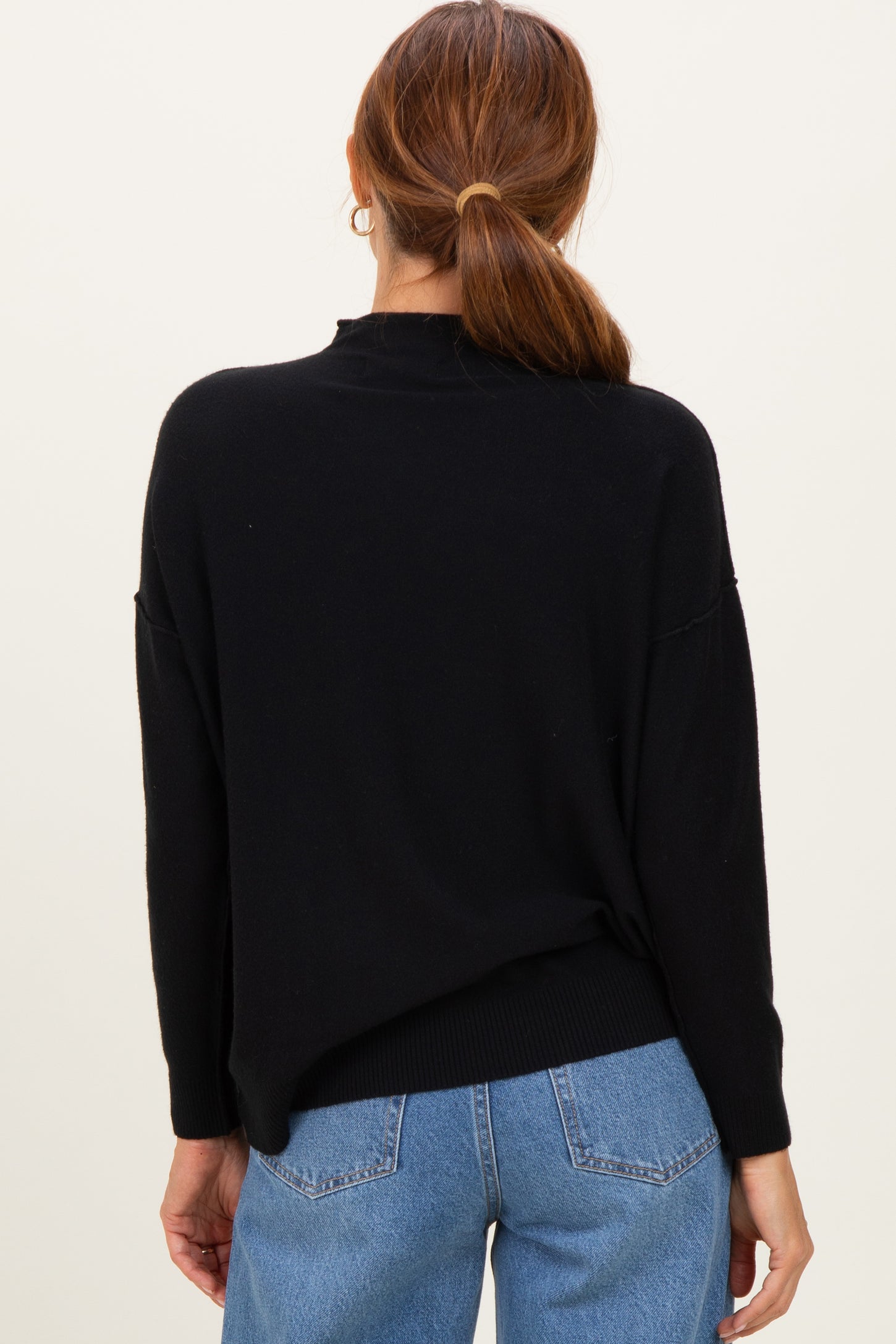 woman wearing a black oversized sweater with a high neckline and dropped shoulders, paired with blue jeans