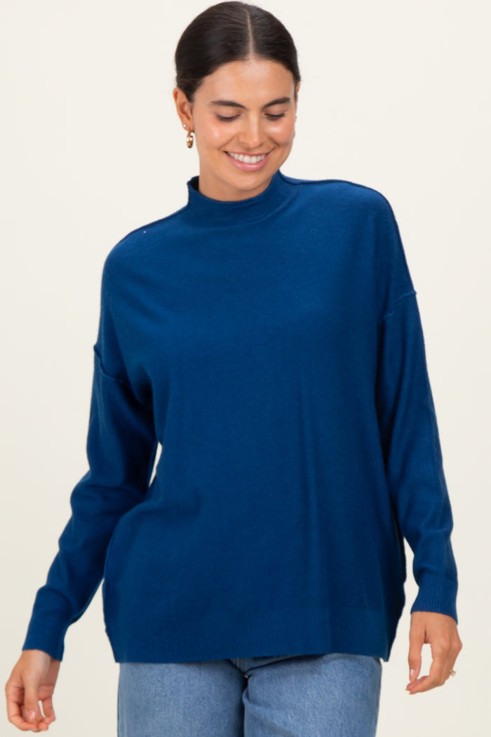 woman wearing a blue high neck sweater with a relaxed fit and long sleeves, smiling against a neutral background