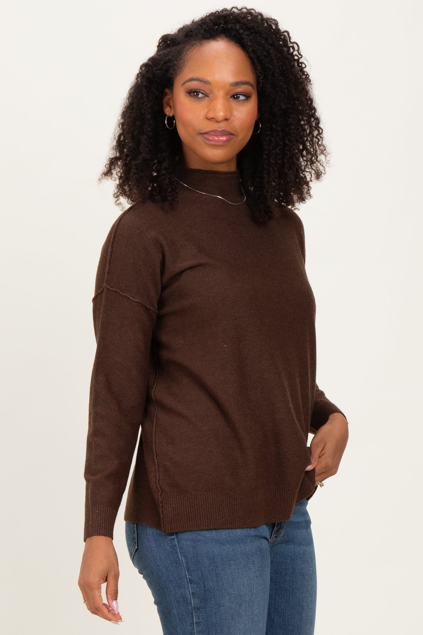 woman wearing a brown turtleneck sweater with relaxed fit and long sleeves paired with blue jeans