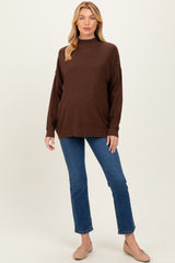 woman wearing a brown maternity sweater with a mock neck and relaxed fit, paired with blue jeans