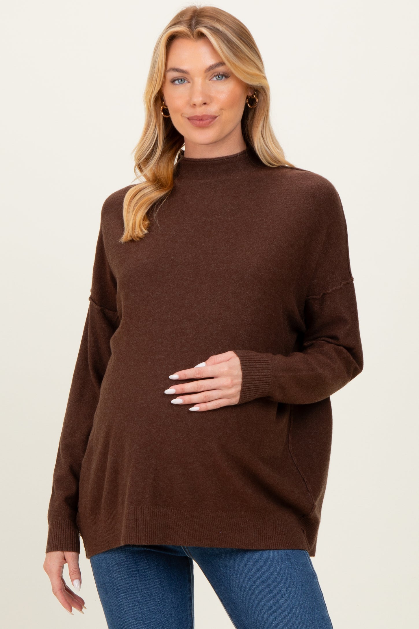 woman wearing a brown oversized maternity sweater and holding her baby bump