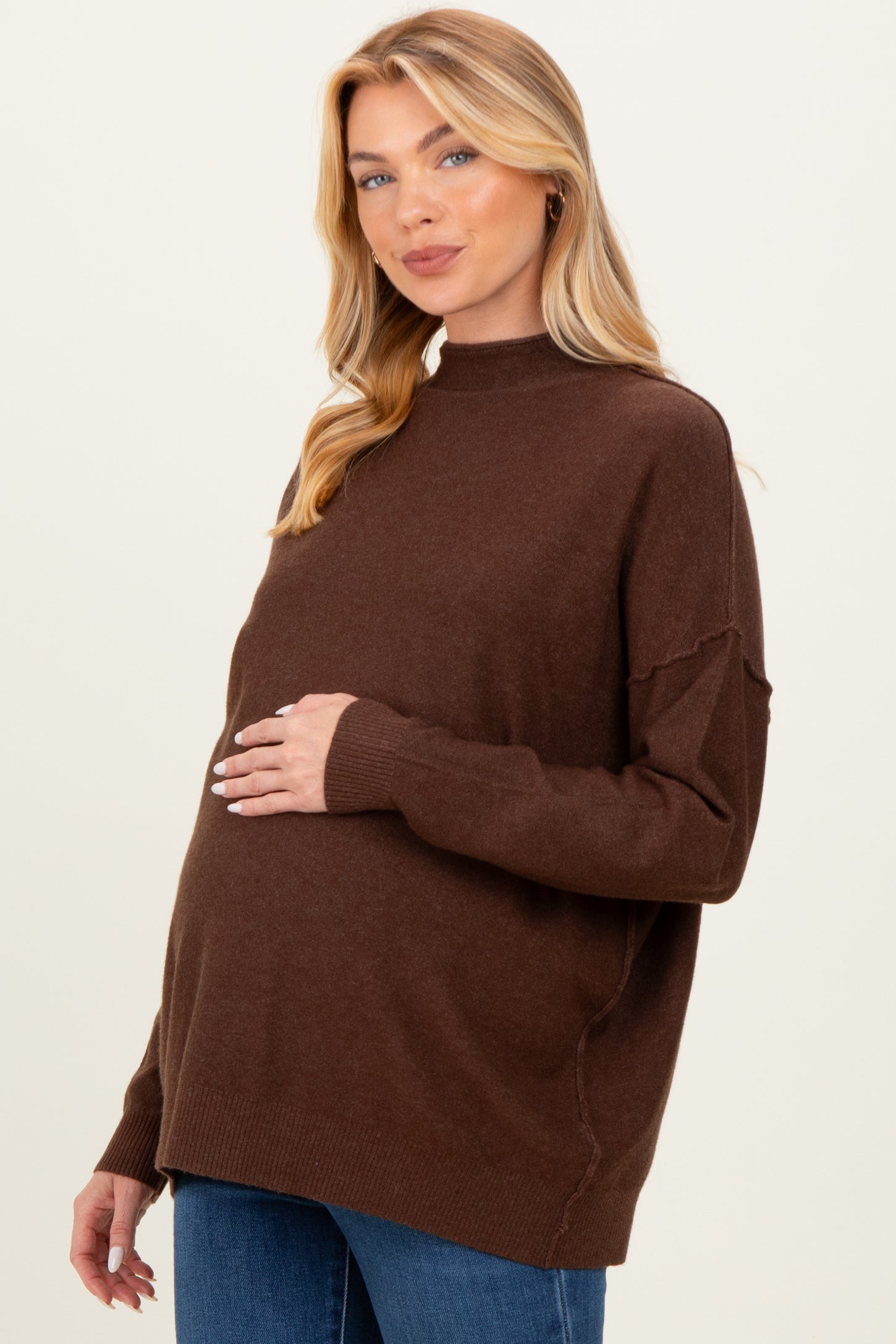 woman wearing a brown maternity sweater with a relaxed fit, gently holding her baby bump