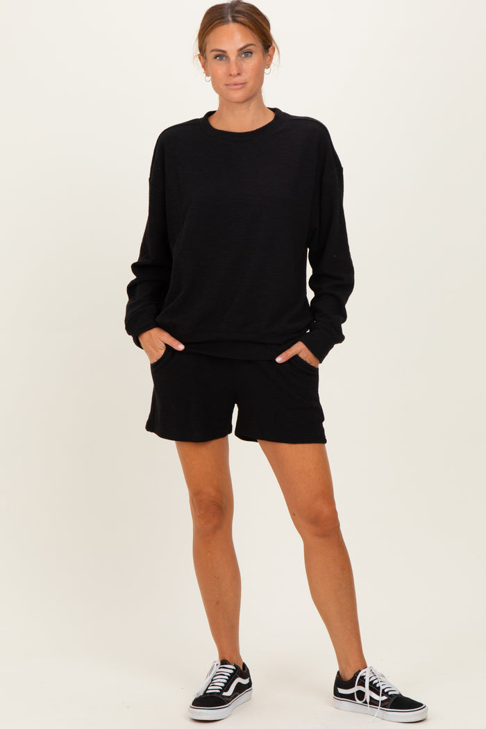woman wearing a black oversized sweatshirt and matching black shorts, standing with hands in pockets