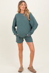 woman wearing a green maternity lounge set with a long sleeve top and matching shorts, featuring relaxed fit and pockets