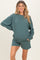 woman wearing a teal maternity sweatshirt and matching shorts, smiling with hands on hips