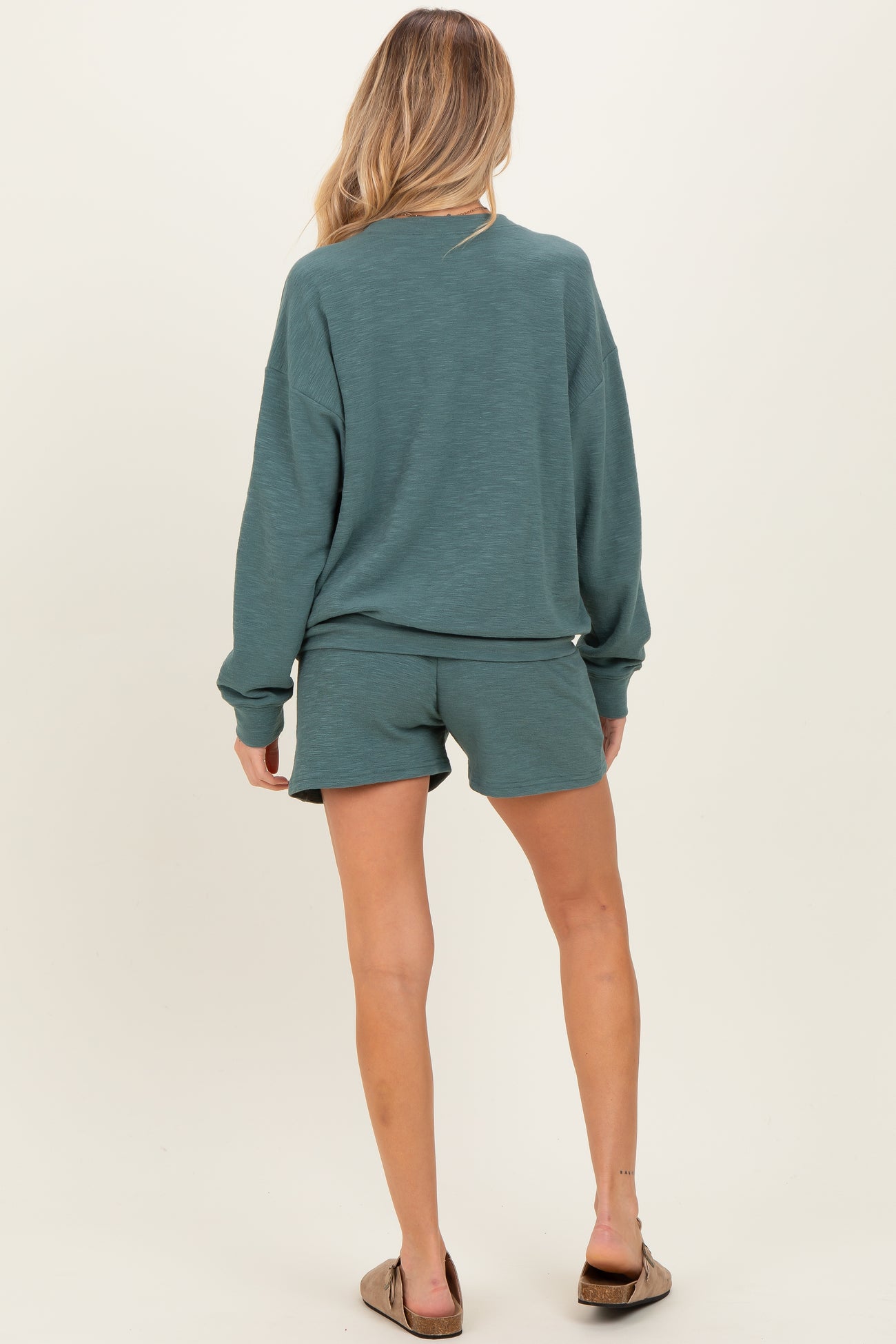 woman wearing a teal maternity sweatshirt and matching shorts, showing a casual and comfortable style from the back
