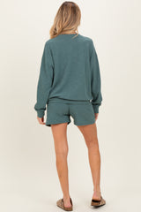 woman wearing a teal maternity sweatshirt and matching shorts, showing a casual and comfortable style from the back