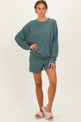 woman wearing a teal oversized sweatshirt and matching shorts, paired with cozy slippers