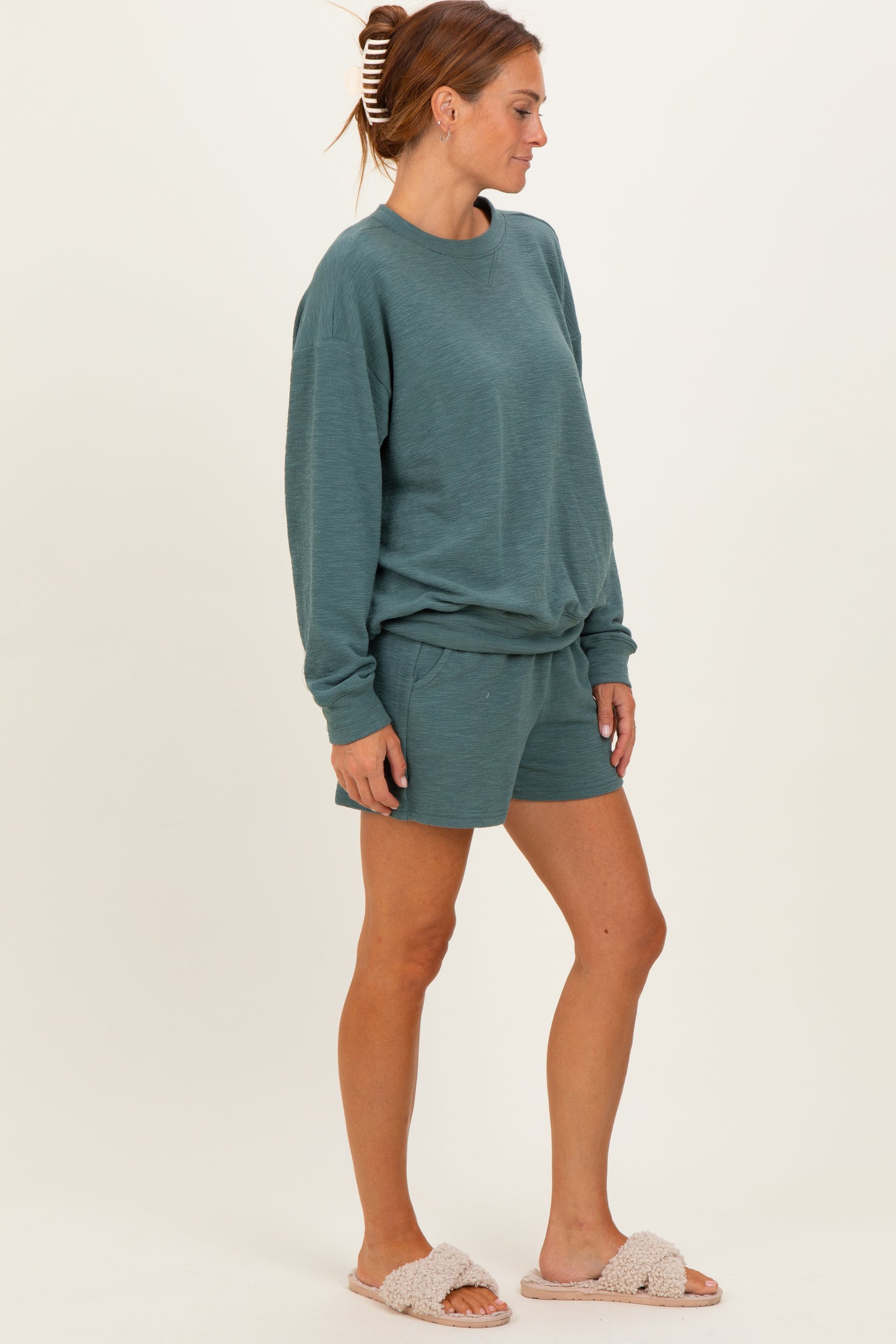 woman wearing a teal long sleeve sweatshirt and matching shorts, paired with light fuzzy slippers